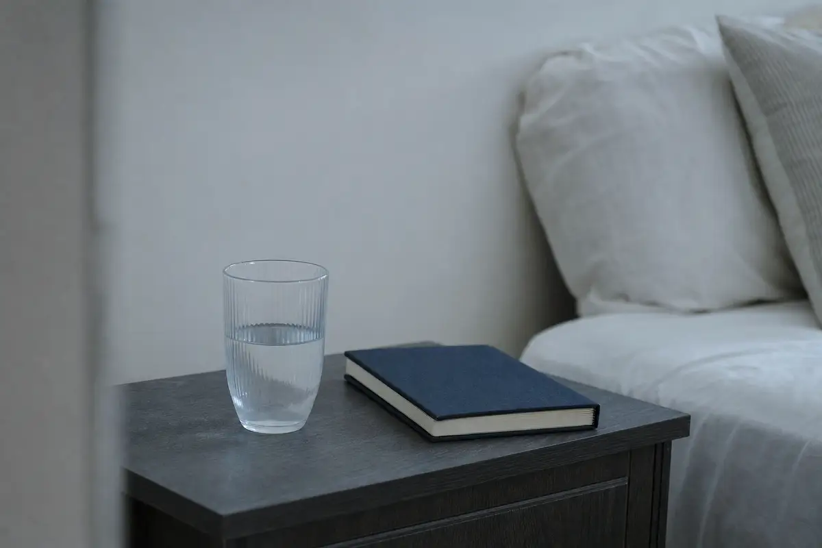 A glass of water and a notebook on a bedside table.