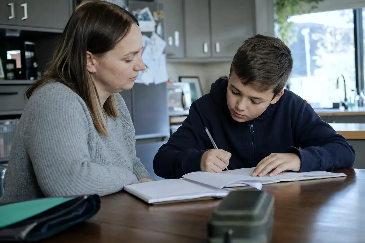 A parent and child at a kitchen table with schoolwork.