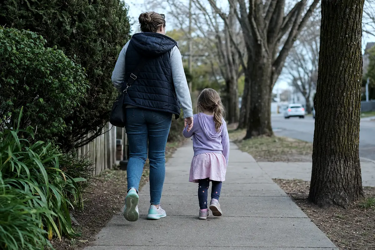 A parent and child walking together on a quiet sidewalk.