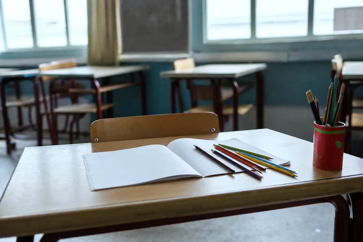 A classroom desk with a notebook and pencils after school.